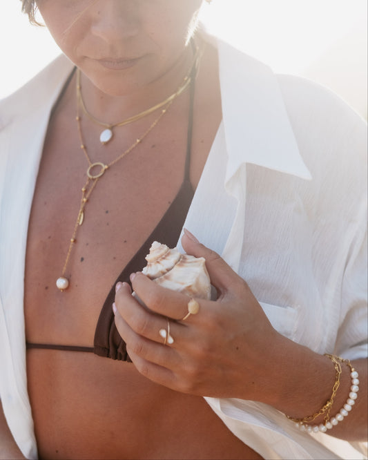 Woman holding a shell with layered necklaces and a white shirt on a bright background