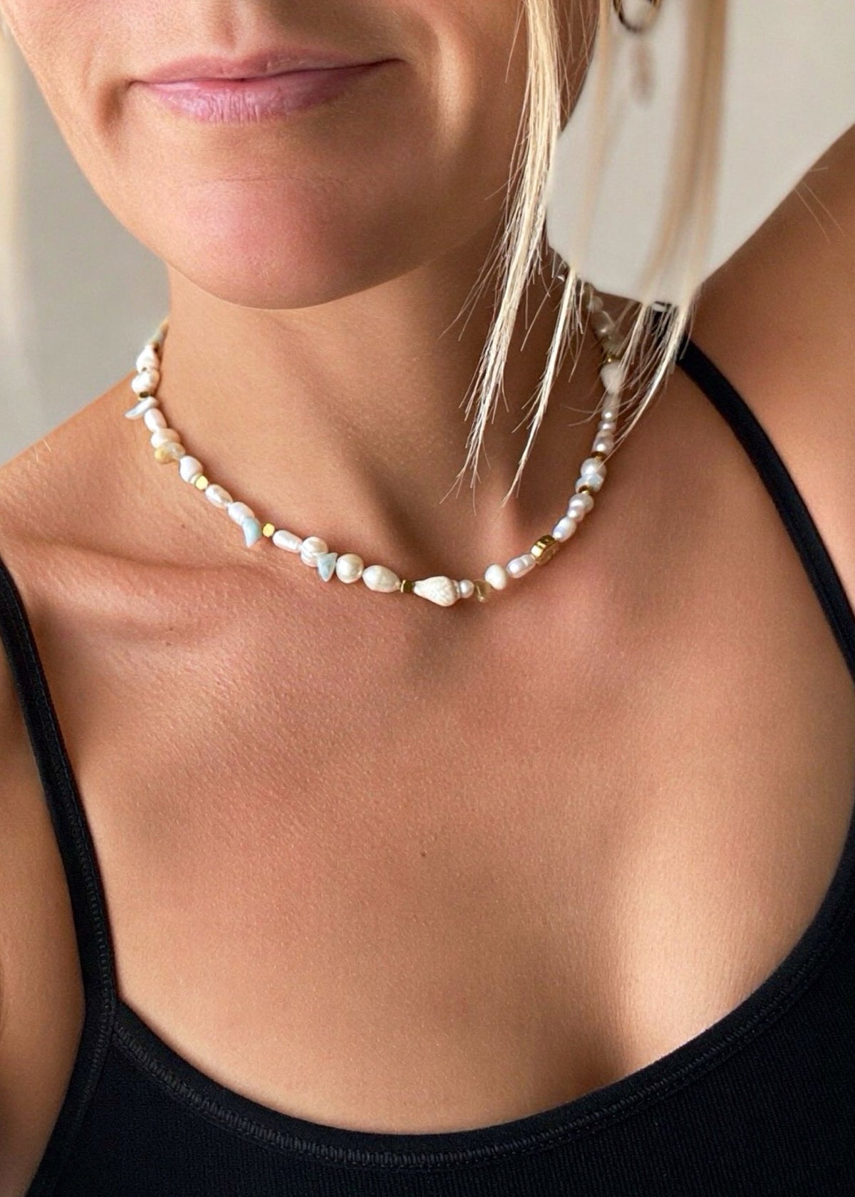 A close-up of a woman wearing a double-strand baroque pearl necklace with small gold spacer beads, paired with a black ribbed tank top.