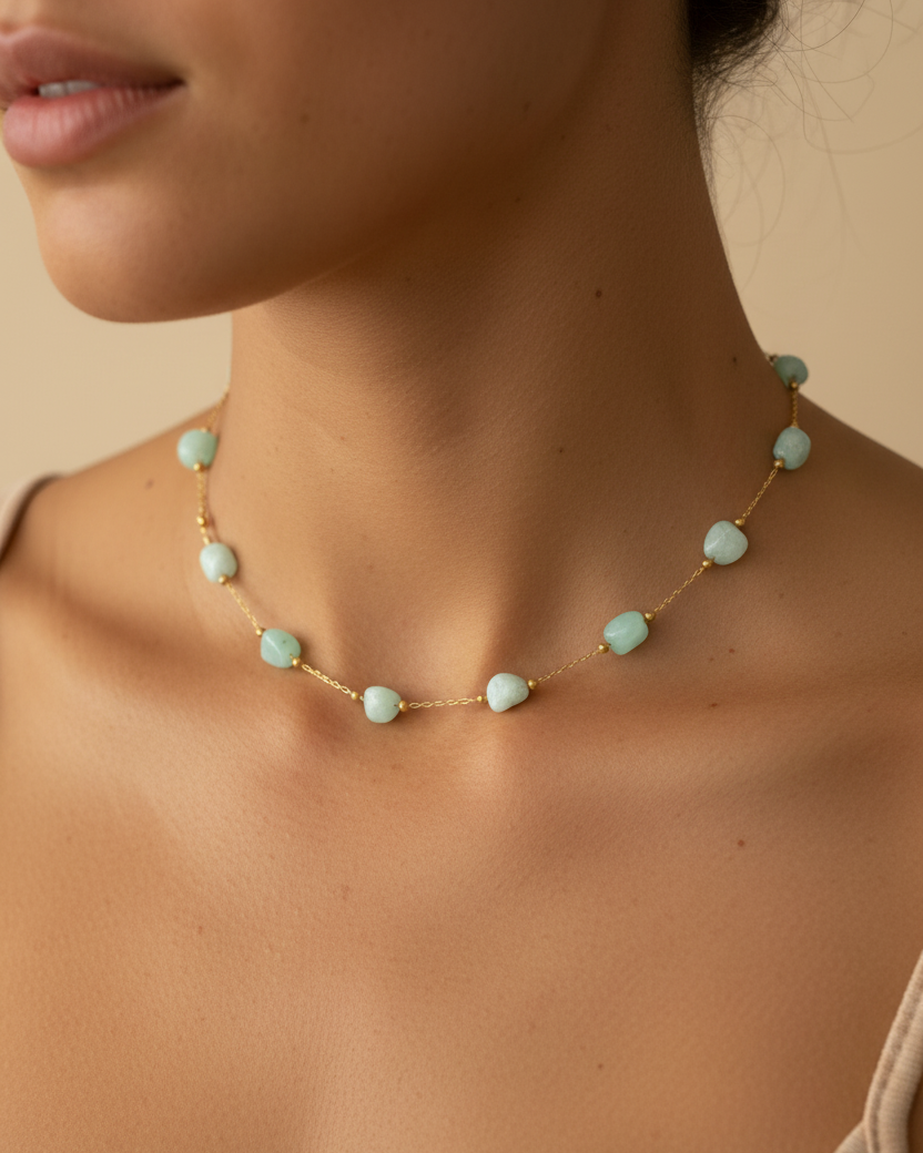 A close-up of a model wearing a delicate gold chain necklace with evenly spaced, light mint green faceted crystals.